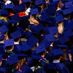 high school graduation with one graduate raising their hand in the middle
